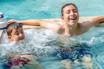 Brothers relax together in a jacuzzi which is attached to an outdoor swimming pool.