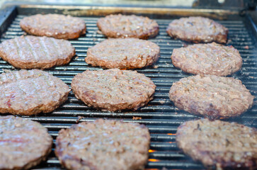Beef burgers cooking on a barbecue.
