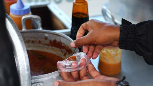 An Indonesian man street food vendor serves a customer in outdoor market. A man preparing a dish called 'Batagor Ikan' to customer on the street of Tarakan.