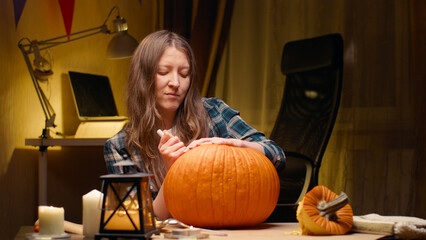 Preparing pumpkin for Halloween. Woman sitting and carving with knife halloween Jack O Lantern pumpkin at home for her family.