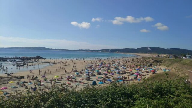 people enjoying a sunny summer day on the beach on the hot afternoon with the blue sky. Panoramic shot. A Lanzada, Pontevedra, Spain