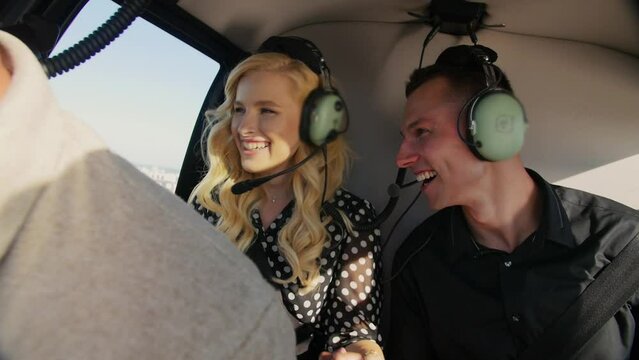 Young couple flying in helicopter.Man and Woman sitting in the cabin of Chopper.Guy smiling with woman at fly in airplane. People in Helicopter