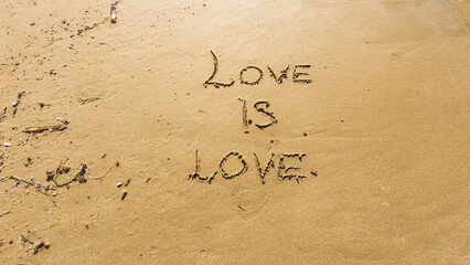 Love is love written on the wet sand of the beach.
