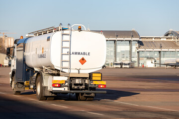 Back view small modern fuel tanker truck driving on airfield taxiway for aircraft refueling....
