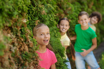 Happy girl and friends looking out of bushes