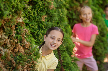 Girl and girlfriend cheerfully looking out of bushes