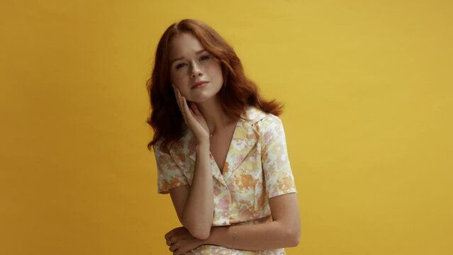 A young ginger white woman understanding and in agreement, in front of a yellow background, wearing a flowery dress.