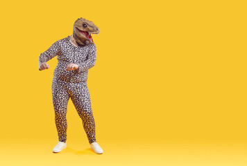 Funny eccentric overweight man dancing in strange dinosaur rubber mask isolated on orange...