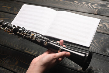 Retro style clarinet in musician hand and music note book flat lay on the wooden desk background.