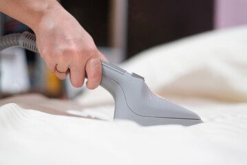Woman ironing bed linen with a steamer close-up.