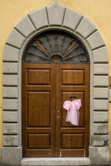 old wooden door with stone arch and a pink ribbon, which says the a girl was born here in italy