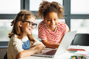 Fototapeta Cheerful  schoolgirls   looking at laptop screen during online lesson obraz