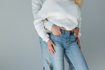 cropped view of couple in white sweaters and jeans posing isolated on grey