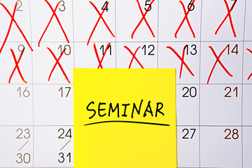 The word Seminar written in black text on a yellow sticky note posted to a calendar page as a reminder. Close up of a personal agenda, top view. Motivational quote
