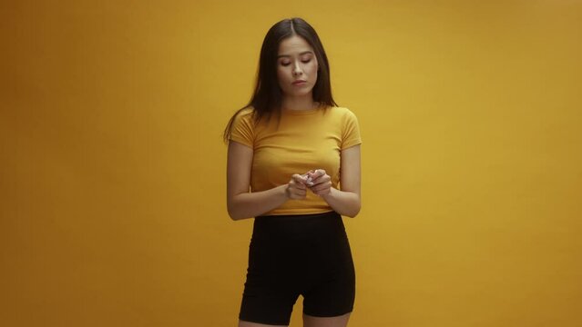 A young Asian woman putting lots of chewing gum into her mouth, in front of a yellow background