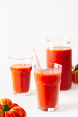 Homemade freshly squeezed tomato juice in glasses and a jug with tomatoes on a white background