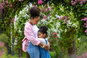 African mother and daughter hugging each other while happily walking under the blossom trellis arch...