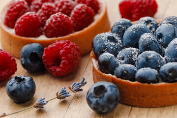 Sweet tarts with fresh raspberries and blueberries on wooden background. Freshly homemade fruit cake, summer berries and sprigs of lavender on a table. macro photography very close up