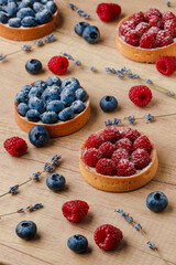 Sweet tarts with fresh raspberries and blueberries on wooden background. Freshly homemade fruit cake, summer berries and sprigs of lavender on a table. Top view