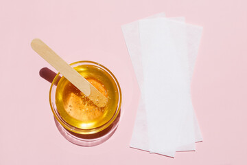 Liquid yellow sugar paste, wooden spatula, depilatory strips on a pink background. Removing unwanted hair. Sugaring. Depilation. Epilation. Beauty. Top view.