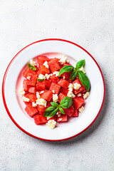 Watermelon salad with feta cheese and basil in plate, gray background. Summer recipe, healthy diet.