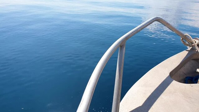 Overlooking bow of metal fishing boat skimming and moving over beautiful sunny day with flat, calm deep blue ocean water