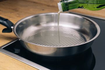 Pouring vegetable oil from green glass bottle in frying pan.