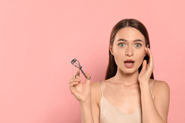 Emotional woman with eyelash curler on pink background, space for text