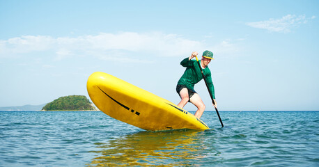 An athlete on a large yellow SUP with a paddle performs a turn trick in turquoise water. Active rest.