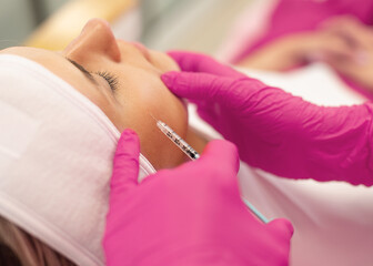 Side view of young woman getting rejuvenation collagen injection into cheekbones lifting skin of...