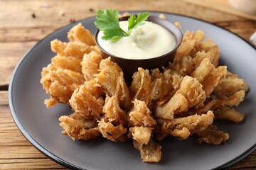 Fried blooming onion with dipping sauce served on wooden table, closeup