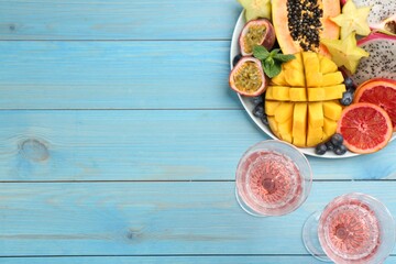 Delicious exotic fruits and wine on light blue wooden table, flat lay. Space for text