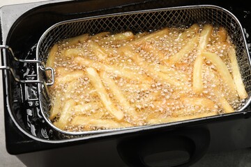 Cooking delicious french fries in hot oil, closeup