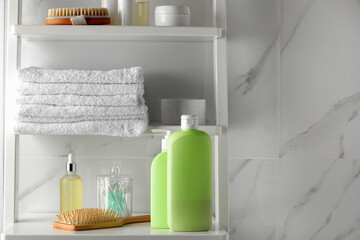Stack of towels, brushes, shampoo and other toiletries on shelves near white marble wall