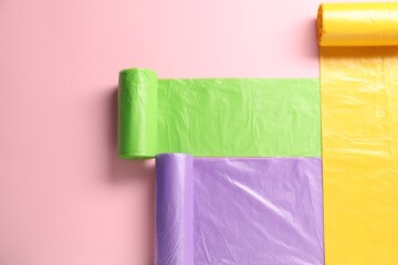 Rolls of different garbage bags on pink background, flat lay