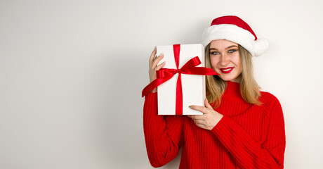 Happy beautiful christmas girl holding gift and smiling wearing santa hat and sweater. Banner in red and white colors.