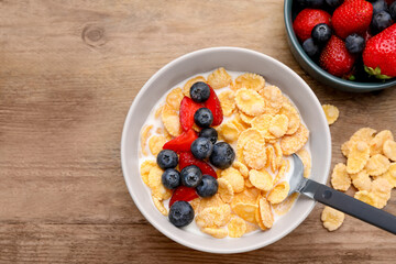 Bowl of tasty crispy corn flakes with milk and berries on wooden table, flat lay. Space for text