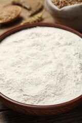 Fototapeta na wymiar Wheat flour in bowl on wooden table, closeup