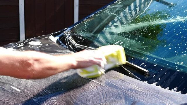  A man washes the hood and windshield of a car outside with a sponge and soapy water on a summer day. car body care, car dry cleaning concept. I clean cars myself