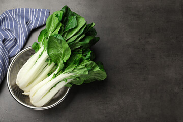 Fresh green pak choy cabbages with water drops in sieve on grey table, top view. Space for text