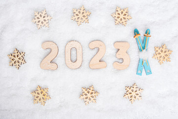 Sports year 2023. Bright blue wooden ski toys, snowflake shape and date 2023 on white snow, flat lay, copy space. Love for skiing. Favorite winter sports concept.