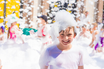 happy little boy with foam on his head, in wet clothes at a foam party or holiday on a sunny hot...