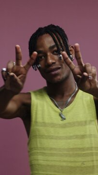 A young black man is showing peace sign on a pink background 