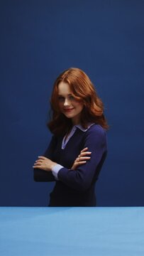 A white ginger woman on a blue background is turning around and winking 