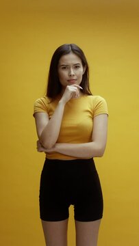 A young asian woman on a yellow background is thinking and nodding head