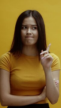 A young asian woman on a yellow background wagging her finger, saying no, disagreeing 