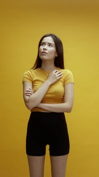A young asian woman on a yellow background pointing up