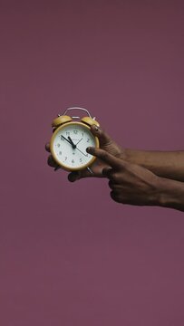 A close-up of a hand displaying the time on an alarm clock against a pink background