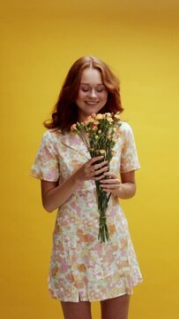 A young white ginger on yellow background receiving bouquet of flowers and being surprised 