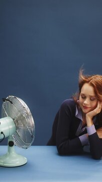 a young white ginger woman on a blue background being hot and turning on the fan